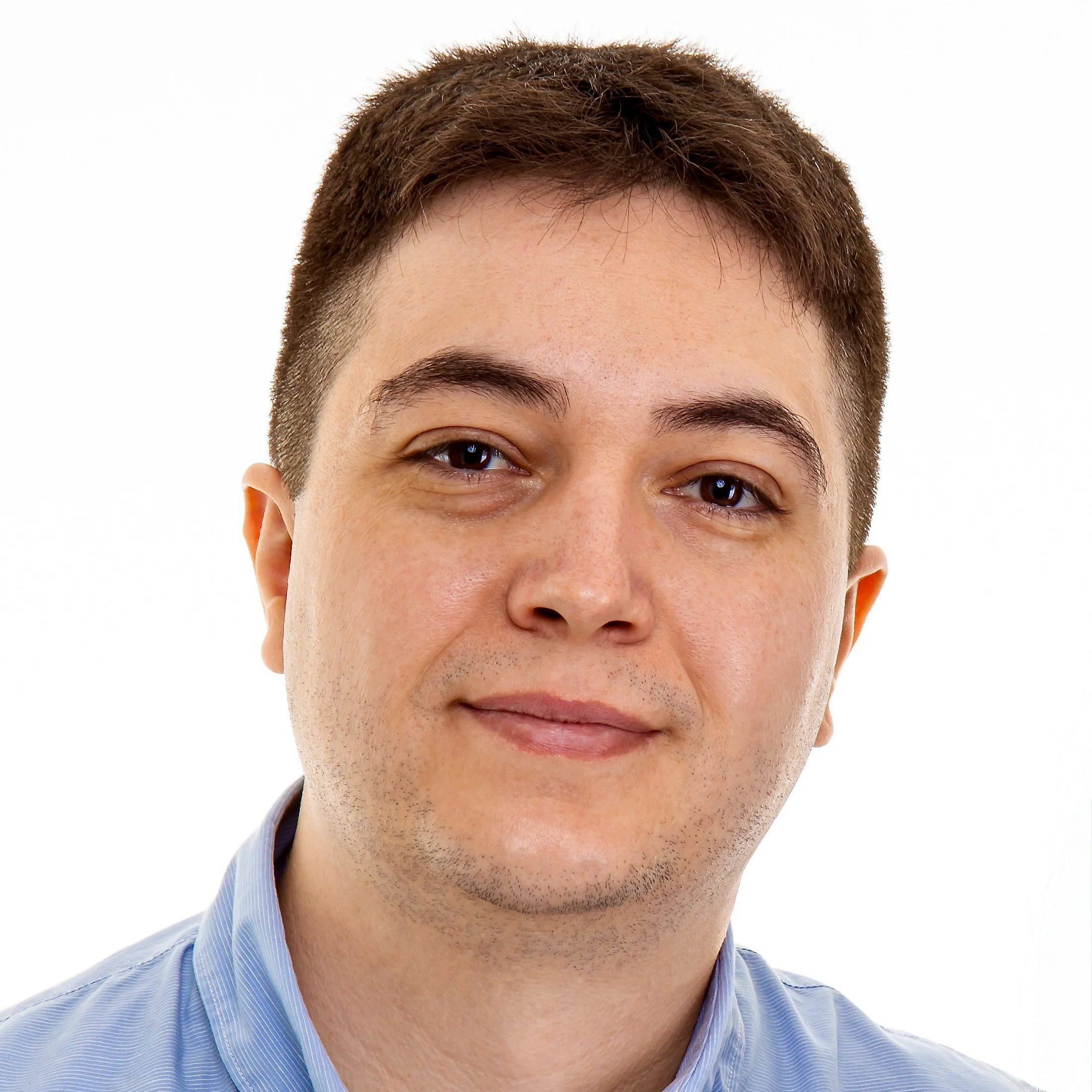 Professional headshot of a man with short brown hair and a light blue button-down shirt, smiling slightly against a white background.