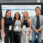 Four researchers posing together in front of a scientific poster presentation at an academic conference hall. The research poster displays University of Guelph branding and is titled 'Gene expression signatures in prepartum peripheral blood leukocytes associated with postpartum health status in dairy cows'.
